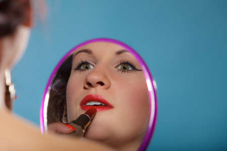 Cosmetic beauty procedures and makeover concept. Closeup part of woman face. Girllooking at mirror applying red lipstick lips makeupの写真素材