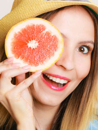Summer vacation. Happy funny girl tourist in hat holding grapefruit citrus fruit on gray.の写真素材