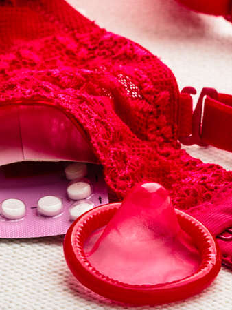 Healthcare medicine, contraception and birth control. Closeup oral contraceptive pills and condom with red lace bra lingerie.の写真素材