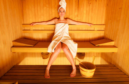 Spa beauty well being and relax concept. Woman in full length white towel sitting relaxed in wooden saunaの写真素材