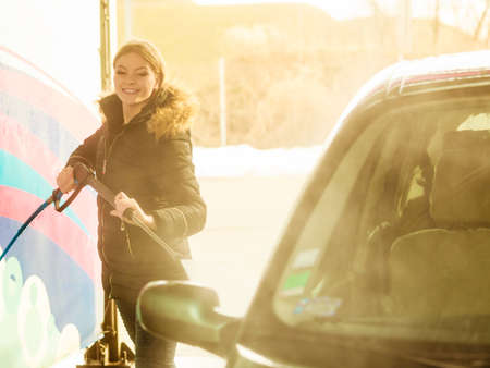 Manual auto wash. Young attractive blonde woman washing the dirty car with foam and pressured water at service station on open airの写真素材
