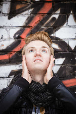 handsome trendy man outdoor in city setting, male model stylish haircut looking up against graffiti wallの写真素材