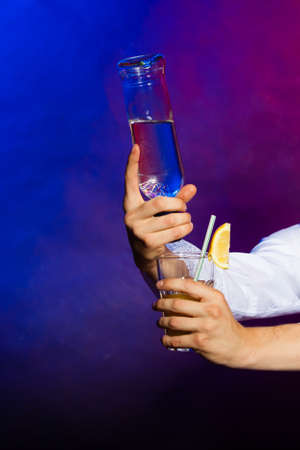 Young man bartender with bottle alcohol pouring a drinkの写真素材