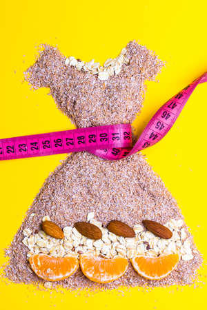 Dieting healthy eating slim down concept. Female dress shape made from cereal bran with measuring tape around thin waistline on yellowの写真素材