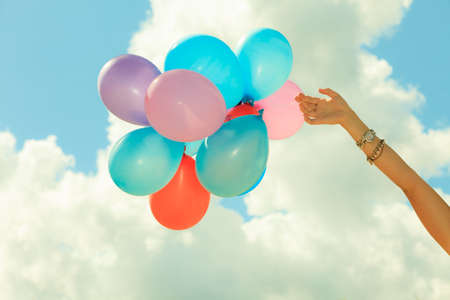Concept of love in summer, freedom and wedding honeymoon. Female hand holding colorful balloons cloudy sky background, outdoorの写真素材