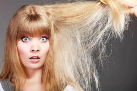Haircare. Blonde woman with her damaged dry hair shocked face expression gray backgroundの写真素材