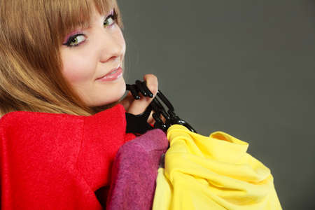 Retail and sale. Blonde girl fashionable woman buying clothes. Client customer holding hangers with vivid color clothingの写真素材