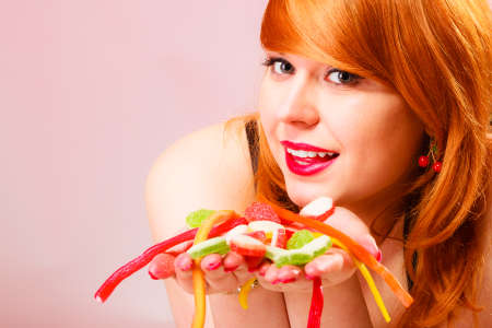 Addiction out of control. Studio shot on pink background. Red haired beautiful woman holding sweets in hands.の写真素材