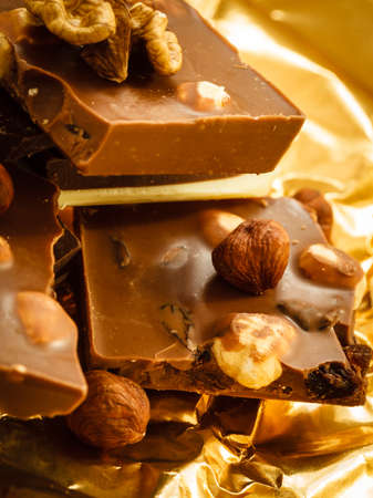 Closeup different sorts chocolate pieces and hazelnuts. Variety of chocolates on golden foil wrapping.の写真素材
