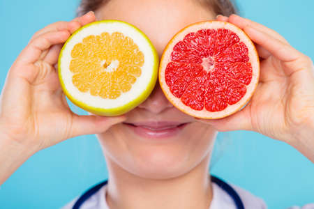 Health concept. Nutritionist doctor holding fruits slices for her eyes on blue. Dietitian...