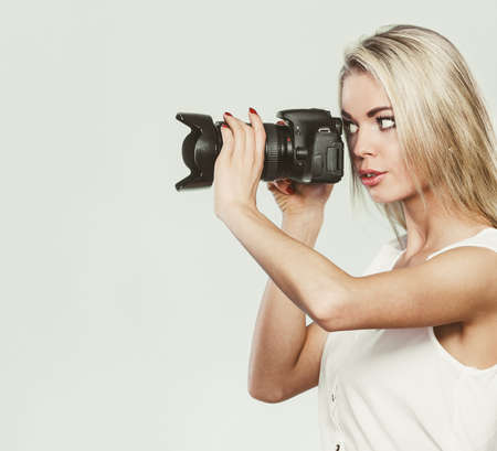 Photographer girl shooting images. Attractive blonde woman taking photos with camera. Filtered photoの写真素材