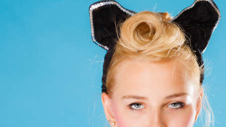 Pin up and retro style coiffure. Blonde woman part face with hairdo black ears on head on blue background in studio.の写真素材