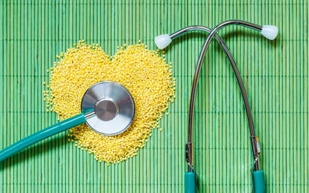 Dieting healthy living concept. Millet groats heart shaped and stethoscope on green mat surface.. Healthy food help lower cholesterol.の写真素材