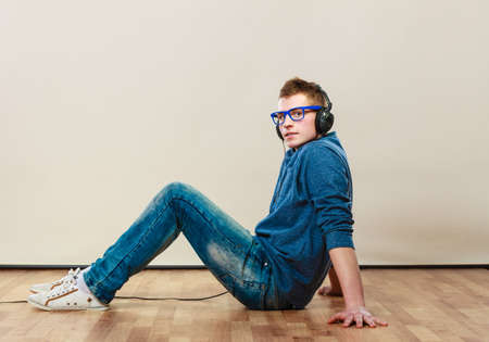 leisure and lifestyle concept. Young hipster man fashion clothes with headphones sitting on floor listening music.の写真素材