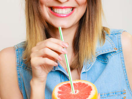Summer vacation. Happy funny girl tourist holding grapefruit citrus drinking juice from fruit on gray.の写真素材