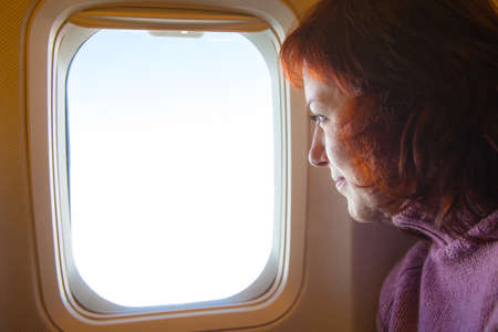 Travelling by air - woman is sitting in the airplane looking  through windowの写真素材