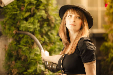 Portrait of young woman outdoors. Retro style fashion girl in black hat and dress on street of the...