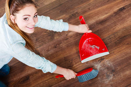 Cleanup housework concept. cleaning woman sweeping wooden floor with red small whisk broom and...