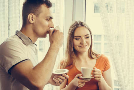 Happiness and healthy relationship concept. Attractive couple drinking tea or coffee together at home, man and woman holding cups with hot beverage at homeの写真素材