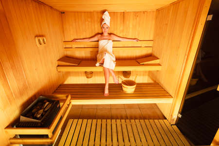 Spa beauty well being and relax concept. Woman in full length white towel sitting relaxed in wooden saunaの写真素材