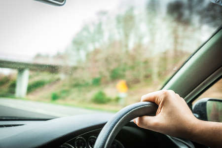Male driver hands holding steering wheel of a car and roadの写真素材