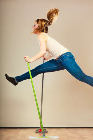 Cleanup housework concept. Funny cleaning lady young woman mopping floor, holding two mops new and old jumpingの写真素材