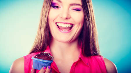 Sweet food sugar make us happy. Smiling woman holds cake chocolate muffin in hand blue backgroundの写真素材