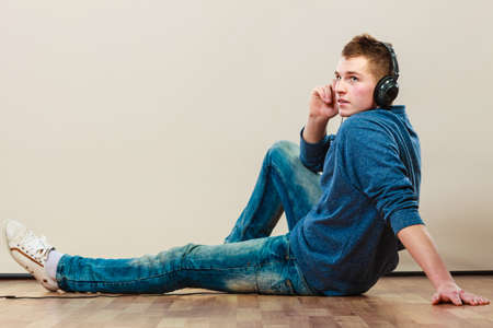leisure and lifestyle concept. Young hipster man fashion clothes with headphones sitting on floor listening music.の写真素材