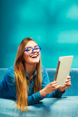 Modern technology education internet concept. Fashion student girl in glasses with tablet relaxing on blue colorの写真素材