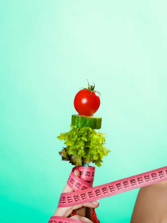 Diet and weight loss concept. Dietician woman hand with vegetarian food and colorful measuring tapes on green blue background.の写真素材
