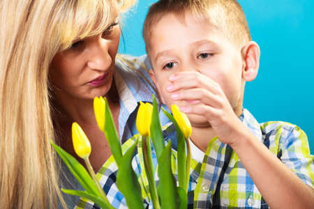 Boy celebrating mother's day. little child lad giving flowers yellow tulips to his mom mother studio shot on blueの写真素材