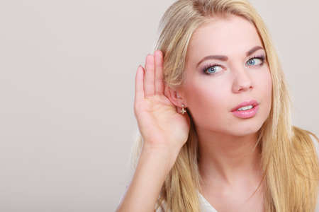 Female hand to ear listening on gray. Gossip girl with palm behind ear spying. Closeup young business woman listening secret.の写真素材