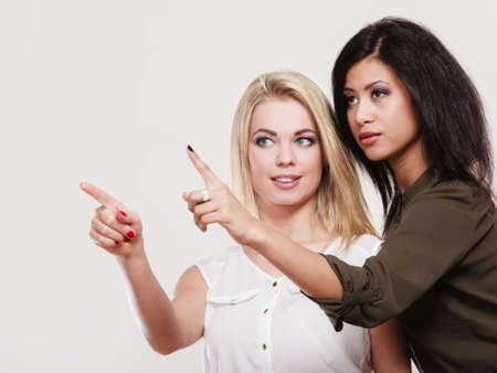Fashion and advertisement concept. Two women caucasian and african pointing into copyspace, studio shotの写真素材