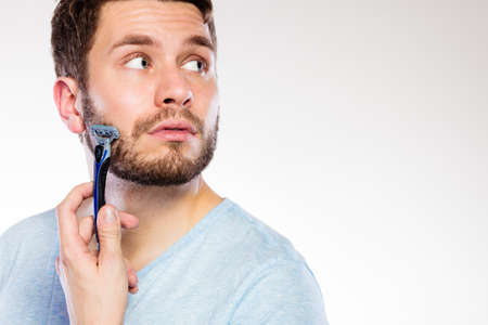 Health beauty and skin care concept. Closeup of male face. Young man guy styling beard holding disposable blue razor blade white background.の写真素材