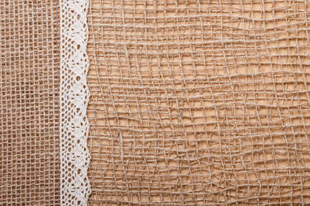 Lace and jute bagging ribbon on brown mesh material, natural burlap backgroundの写真素材