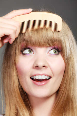 Fashion beauty and haircare concept. Closeup young woman refreshing her hairstyle girl combing her hair fringe with wooden combの写真素材