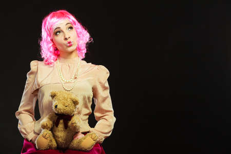 Mental disorder concept. Young childlike woman wearing like puppet doll sitting with teddy bear toy on red couch dark black backgroundの写真素材