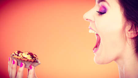 Bakery, sweet food and people concept. Woman face profile wide open mouth holds cake cupcake in hand...