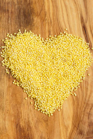 Dieting healthcare concept. Millet groats heart shaped on wooden surface. Healthy food gluten-free and highly alkaline.の写真素材