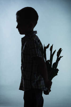Holiday mother's day concept. Little boy silhouette has prepared surprise present for mum, flowers...