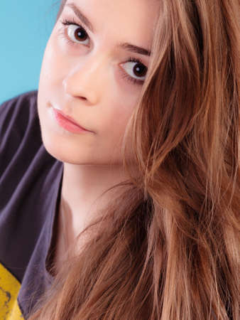 Beautiful female young woman teen girl with brown long healthy loose hair blue backgroundの写真素材