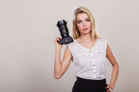 Photographer girl shooting images. Lovely blonde woman with professional camera on gray background