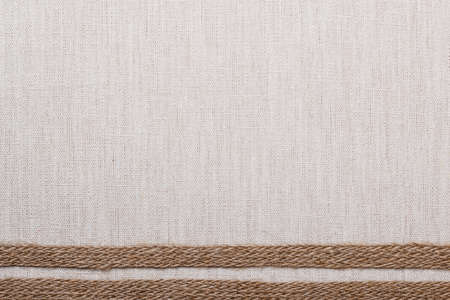 Jute bagging ribbon on bright fabric textile material, natural linen backgroundの写真素材