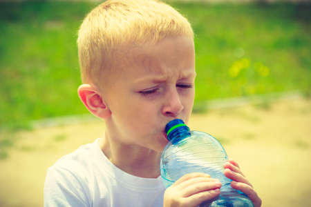 Little thirsty boy child drink water from plastic bottle, outdoorの写真素材