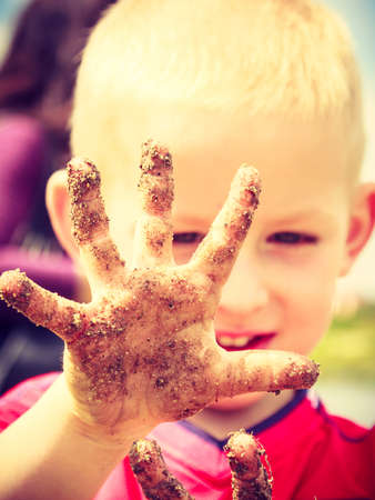Child little blonde boy kid playing outdoor showing dirty muddy hands. Happy childhood.の写真素材