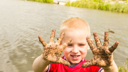 Child little blonde boy kid playing outdoor showing dirty muddy hands. Happy childhood.