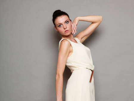 Glamour girl in white dress on gray. Fashion young woman hait bun posing. Studio photoの写真素材