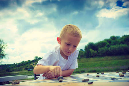 Draughts board game. Little boy clever child kid playing checkers thinking outdoor in the park. Childhood and developmentの写真素材