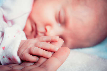 parenting and love concept. Closeup tiny hand the sleeping baby girl in the palm of motherの写真素材