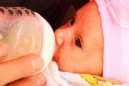 Parenting concept. Happy young father feeding newborn baby girl with milk bottle on couch at homeの写真素材